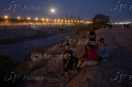 Migrants sit along the bank of the Rio Grande river in Ciudad Juarez