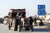 Displaced people who fled from Aleppo countryside, ride on a vehicle with belongings past a road sign of Aleppo in Tabqa