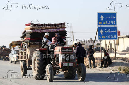 Displaced people who fled from Aleppo countryside, ride on a vehicle with belongings past a road sign of Aleppo in Tabqa