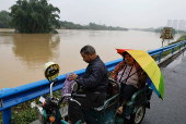 Residents ride on a scooter near a flooded river, following heavy rainfall in Qingyuan