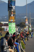 Job seekers sit beneath campaign posters for the South African general elections, in Cape Town
