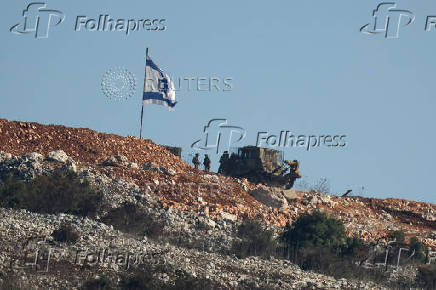 Israeli soldiers stand under an Israeli flag in southern Lebanon, near the Israel-Lebanon border