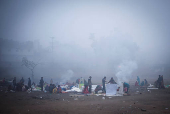 People sit next to a fire at an open ground on a foggy winter morning in the old quarters of Delhi