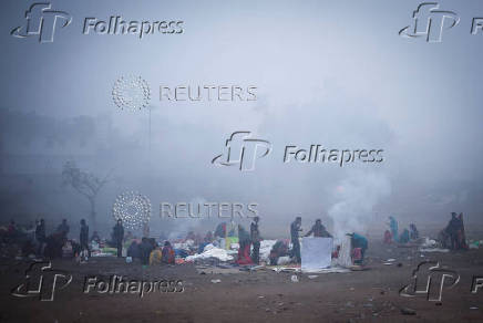 People sit next to a fire at an open ground on a foggy winter morning in the old quarters of Delhi