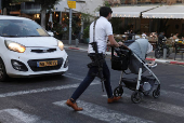 An armed man pushes his kid's cart, amid the Israel-Hamas conflict, in Tel Aviv