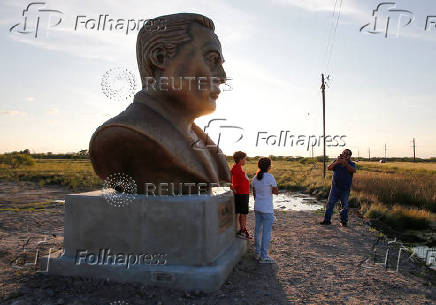 Joel Guiterrez photographs his grandchildren next to a bust of SpaceX founder Elon Musk, erected near the company's launch pad facility, in Brownsville