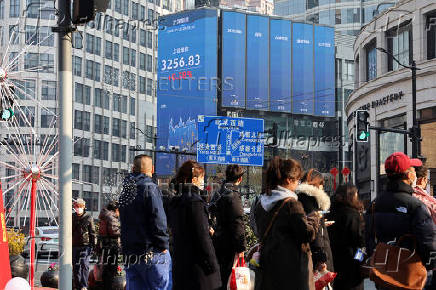 Pedestrians wait for a street signal on a sidewalk as an electronic billboard shows the Shanghai stock index in Shanghai