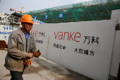 FILE PHOTO: FILE PHOTO: A person walks past by a gate with a sign of Vanke at a construction site in Shanghai