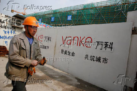 FILE PHOTO: FILE PHOTO: A person walks past by a gate with a sign of Vanke at a construction site in Shanghai