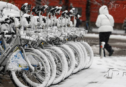 Woman walks past bicycles for rent during a snowfall in Kyiv