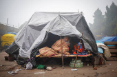 A man wrapped himself in a blanket sits inside a temporary shelter on a foggy winter morning in the old quarters of Delhi