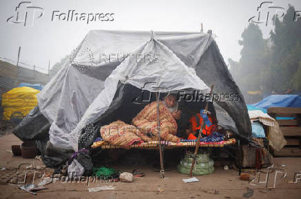 A man wrapped himself in a blanket sits inside a temporary shelter on a foggy winter morning in the old quarters of Delhi