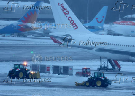 Staff use tractors to help clear snow from around aircraft after overnight snowfall caused the temporary closure of Manchester Airport in Manchester