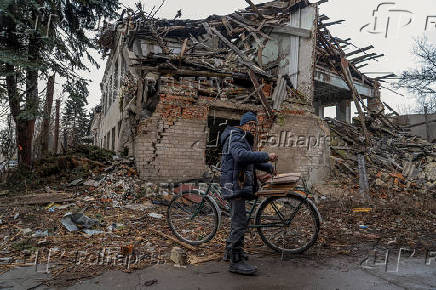 Mykola attaches firewood to his bicycle in front of a building damaged by Russian military strikes in Pokrovsk