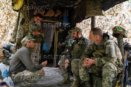 Ukrainian servicemen speak to each other next to a dugout at their position in a front line in Donetsk region