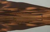 A man walks near sand dunes partially covered by floodwaters, after rare rainfall hit the area last September, in Merzouga