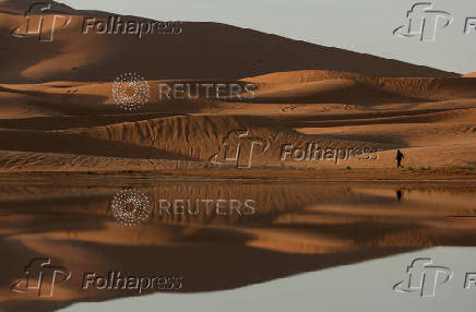 A man walks near sand dunes partially covered by floodwaters, after rare rainfall hit the area last September, in Merzouga