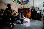 Tofik looks on as Nasreen sticks artificial gems on an embroidered cloth during her part time job at her residence in Loni town in the northern state of Uttar Pradesh