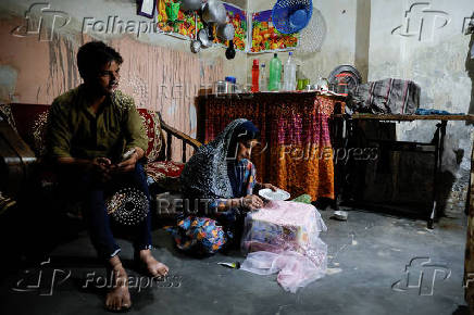 Tofik looks on as Nasreen sticks artificial gems on an embroidered cloth during her part time job at her residence in Loni town in the northern state of Uttar Pradesh