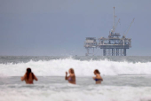 People swim in front on an offshore oil rig platform in Huntington Beach