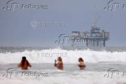 People swim in front on an offshore oil rig platform in Huntington Beach