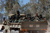 Israeli soldiers gesture from a military truck as it maneuvers near the Israel-Gaza border