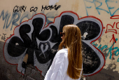 A woman walks past a graffiti on the wall that says 