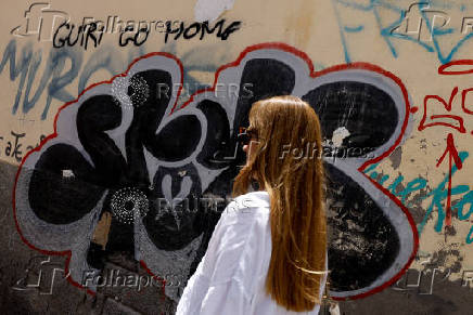 A woman walks past a graffiti on the wall that says 