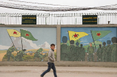 A boy walks past drawings on a wall depicting Kurdish People's Protection Units (YPG) and Kurdish female fighters of the Women's Protection Unit (YPJ) flags in Qamishli