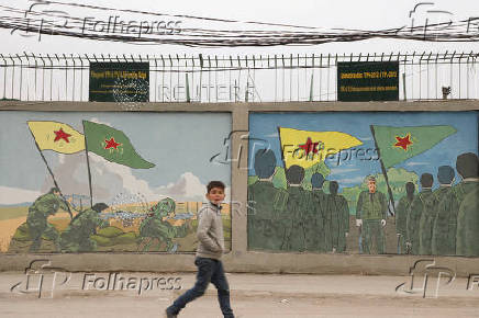 A boy walks past drawings on a wall depicting Kurdish People's Protection Units (YPG) and Kurdish female fighters of the Women's Protection Unit (YPJ) flags in Qamishli