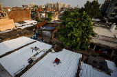 Painters apply solar reflective paint on roofs of shanties in a slum area in Ahmedabad