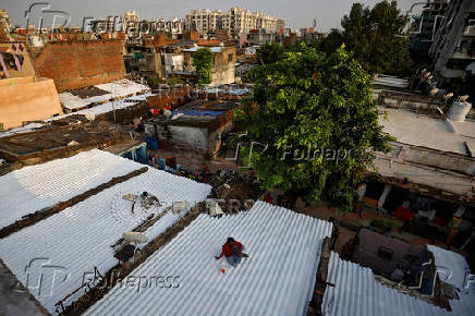 Painters apply solar reflective paint on roofs of shanties in a slum area in Ahmedabad