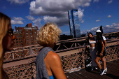 People pose for photographs as other walk on the Brooklyn Bridge in New York City