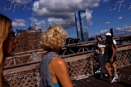 People pose for photographs as other walk on the Brooklyn Bridge in New York City