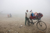 A vendor selling bedsheets loads them onto his bicycle on a foggy and cold winter morning in New Delhi