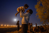 A migrant man plays with his son along the bank of the Rio Grande river in Ciudad Juarez