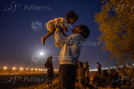A migrant man plays with his son along the bank of the Rio Grande river in Ciudad Juarez