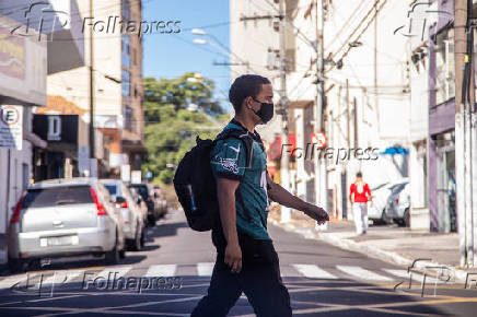 Rapaz com mscara de proteo realiza travessia em faixa de pedestre