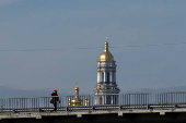 Man walks along a bridge while a bell tower of the Kyiv-Pechersk Lava is seen on a background in Kyiv