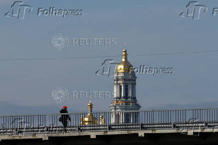 Man walks along a bridge while a bell tower of the Kyiv-Pechersk Lava is seen on a background in Kyiv