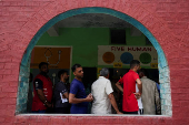 People wait in line outside a polling station to vote during the state assembly elections, in Karnal