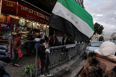 Boy eats, next to the flag adopted by the new Syrian rulers, in Damascus