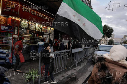 Boy eats, next to the flag adopted by the new Syrian rulers, in Damascus