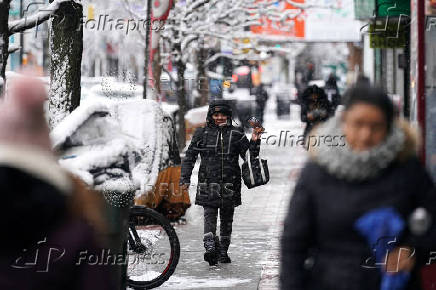 A person walks along the sidewalk whilst on a video call during the city's first snowfall of the season, on the first day of winter in the Queens borough of New York City