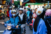 People ride on a motorbike at a night market in Taipei
