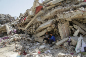 Palestinians sit at the rubble of a residential building destroyed by Israeli strikes, amid the ongoing conflict between Israel and Hamas, in the northern Gaza Strip