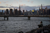 The sun sets behind the Manhattan skyline in the Brooklyn borough of New York City