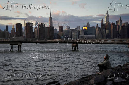 The sun sets behind the Manhattan skyline in the Brooklyn borough of New York City