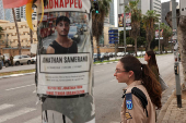 People wait to cross the road, near a poster with a picture of a hostage, who was kidnapped during the deadly October 7 attack on Israel by Palestinian Islamist group Hamas, in Tel Aviv