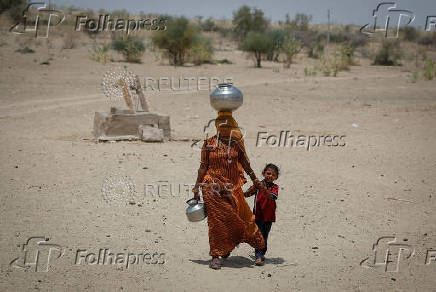 A woman walks back towards her home after filling water from a shallow well in the desert area in Barmer